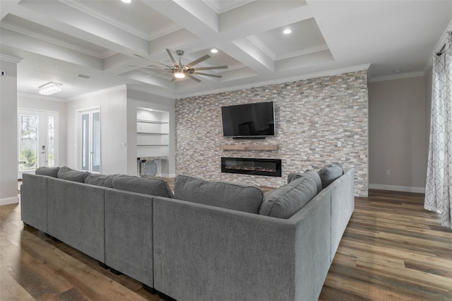 living room with crown molding, dark wood-type flooring, coffered ceiling, a stone fireplace, and beamed ceiling