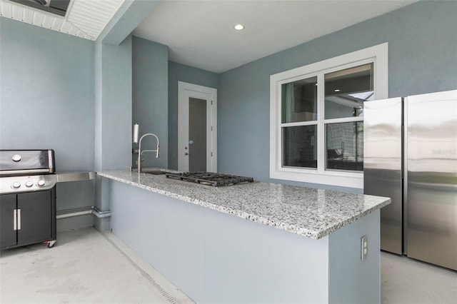 kitchen featuring appliances with stainless steel finishes, kitchen peninsula, sink, and light stone countertops