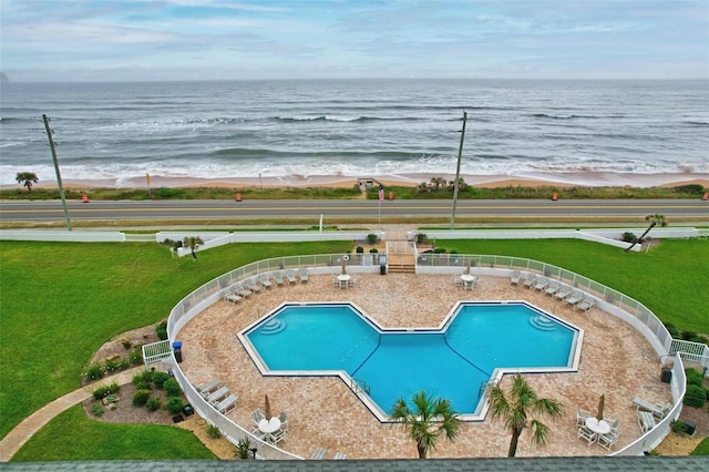 view of pool featuring a view of the beach, a yard, and a water view