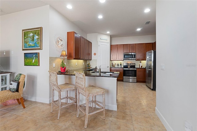 kitchen with a breakfast bar, sink, appliances with stainless steel finishes, kitchen peninsula, and backsplash