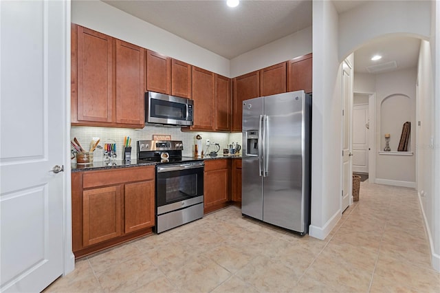 kitchen featuring light tile patterned flooring, stainless steel appliances, dark stone counters, and backsplash