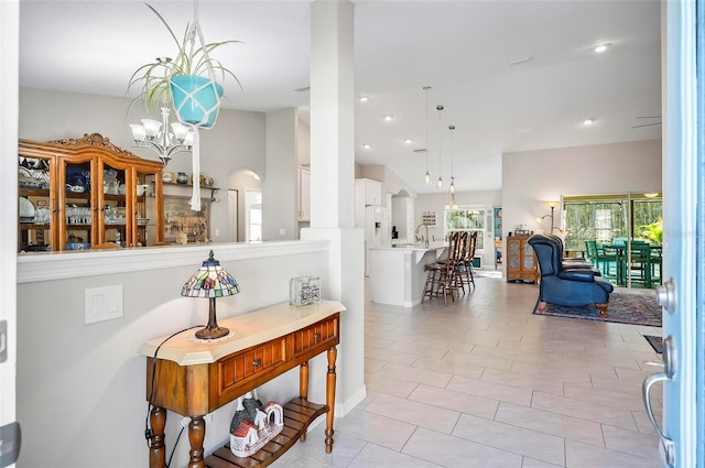 hall with an inviting chandelier, lofted ceiling, sink, and light tile patterned floors