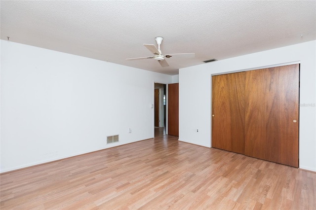 unfurnished bedroom with ceiling fan, a closet, a textured ceiling, and light wood-type flooring