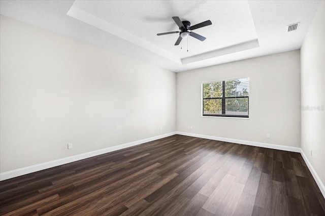 unfurnished room featuring a tray ceiling, dark hardwood / wood-style flooring, and a textured ceiling