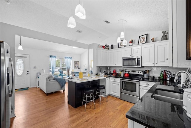 kitchen with white cabinetry, lofted ceiling, stainless steel appliances, and decorative light fixtures