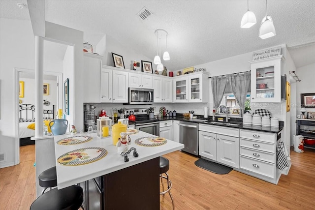 kitchen with a breakfast bar, sink, white cabinetry, pendant lighting, and stainless steel appliances