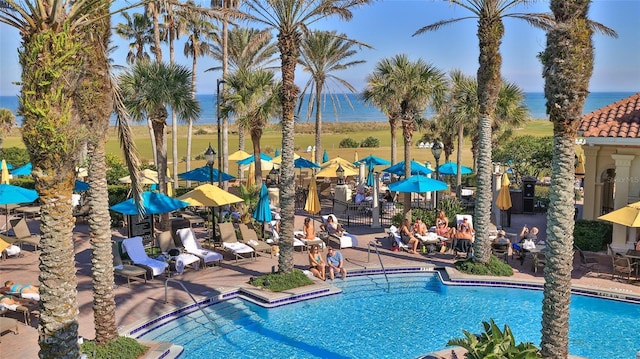 community pool featuring a water view, a patio area, and fence