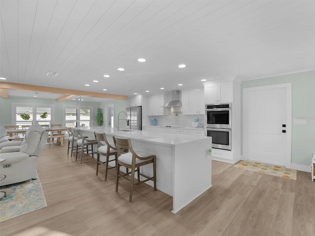 kitchen with appliances with stainless steel finishes, white cabinetry, a kitchen breakfast bar, wall chimney range hood, and a spacious island