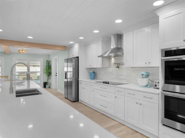 kitchen with wall chimney range hood, sink, white cabinetry, stainless steel appliances, and decorative backsplash