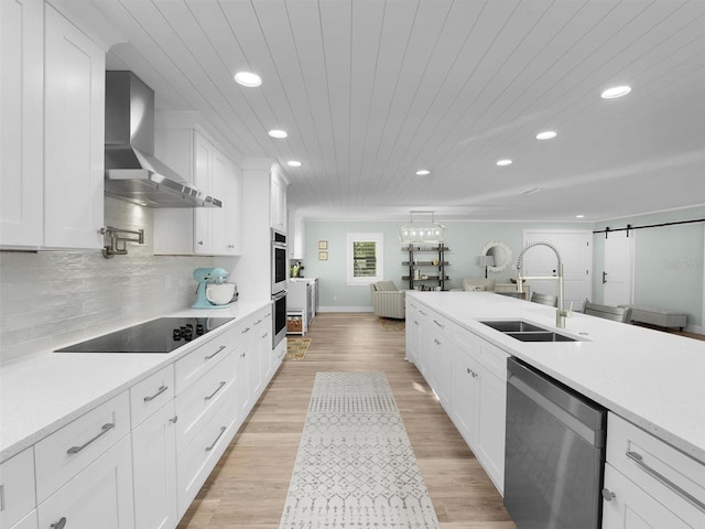 kitchen with sink, wall chimney range hood, white cabinetry, stainless steel appliances, and a barn door