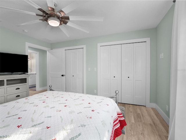 bedroom with two closets, light hardwood / wood-style flooring, and ceiling fan