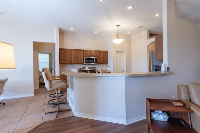 kitchen with stainless steel appliances, hanging light fixtures, a kitchen bar, and kitchen peninsula