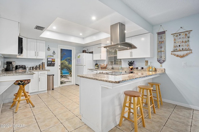 kitchen featuring island exhaust hood, white refrigerator, light stone counters, white cabinets, and light tile patterned flooring