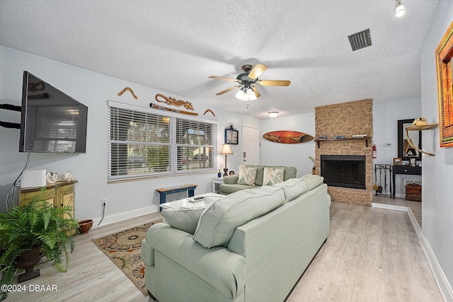 living room with a fireplace, a textured ceiling, light hardwood / wood-style flooring, and ceiling fan