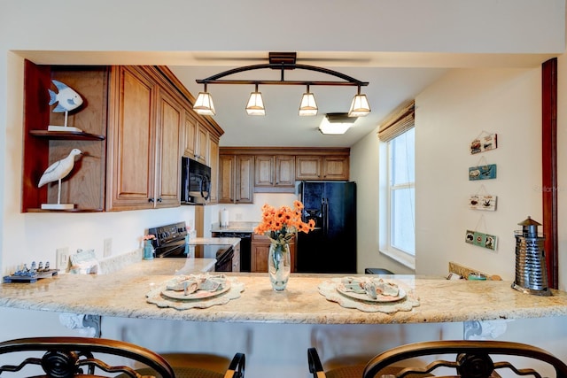 kitchen featuring decorative light fixtures, black appliances, a kitchen bar, kitchen peninsula, and light stone countertops