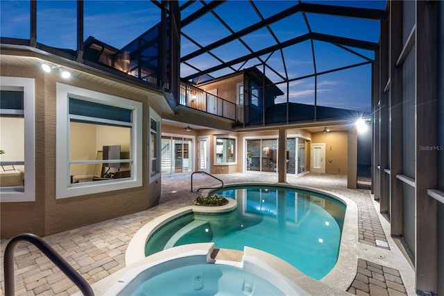 pool at dusk with an in ground hot tub, a lanai, ceiling fan, and a patio