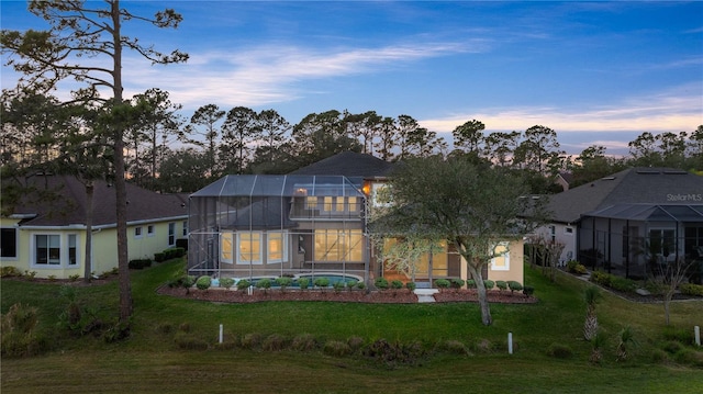 back house at dusk with a yard and glass enclosure