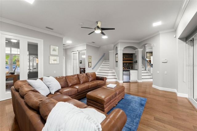 living room featuring crown molding, ceiling fan, hardwood / wood-style floors, decorative columns, and a barn door