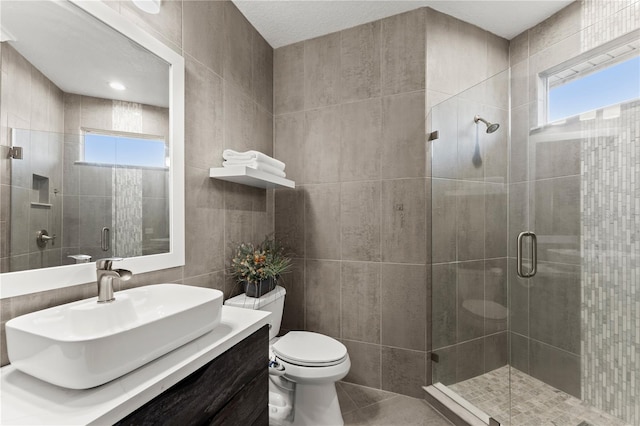 bathroom with tile patterned floors, toilet, tile walls, vanity, and a shower with door