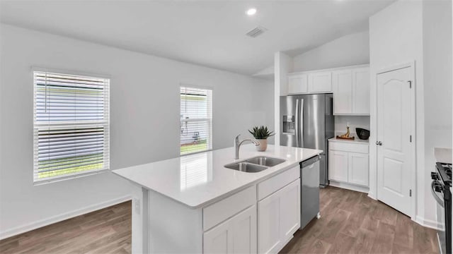 kitchen featuring lofted ceiling, sink, appliances with stainless steel finishes, white cabinetry, and a center island with sink