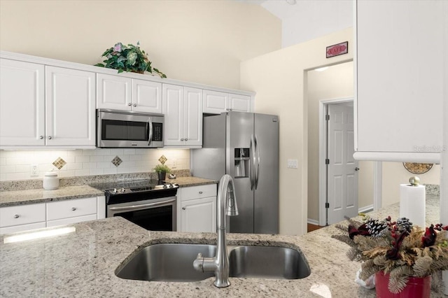 kitchen featuring appliances with stainless steel finishes, sink, white cabinets, backsplash, and light stone countertops