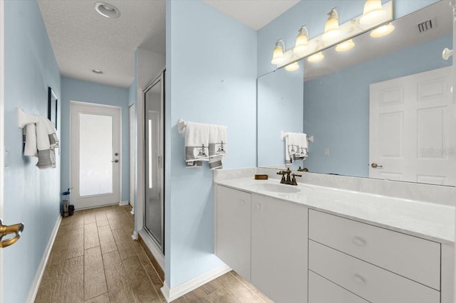 bathroom with vanity, a shower with door, hardwood / wood-style floors, and a textured ceiling