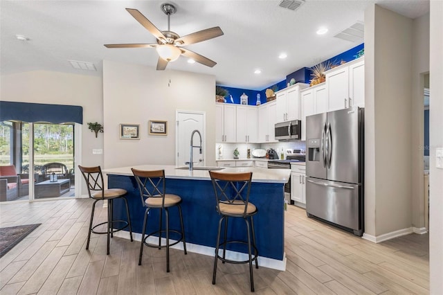 kitchen with white cabinetry, sink, stainless steel appliances, and a center island with sink