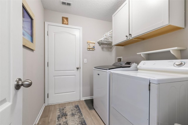 washroom with cabinets, a textured ceiling, independent washer and dryer, and light hardwood / wood-style flooring