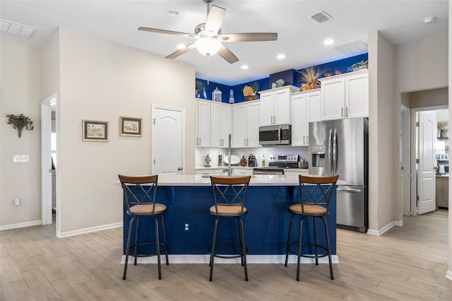 kitchen featuring white cabinetry, a center island with sink, stainless steel appliances, light hardwood / wood-style floors, and a kitchen bar