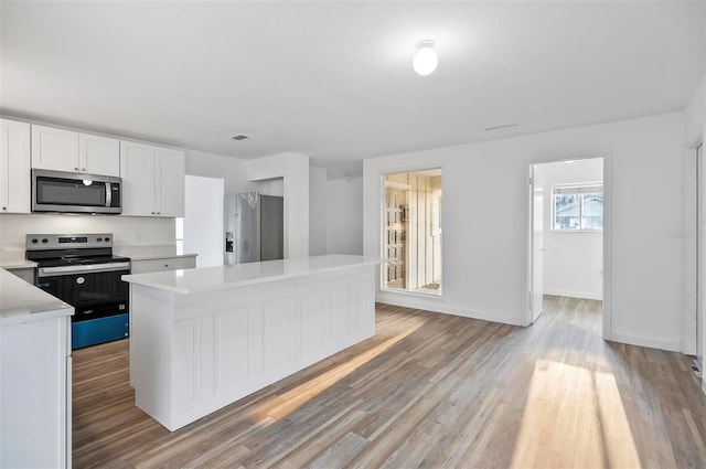 kitchen with light wood-type flooring, a kitchen island, white cabinets, and appliances with stainless steel finishes