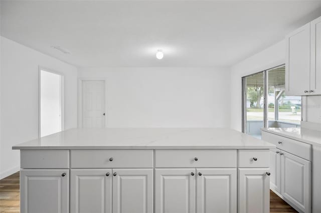 kitchen with a kitchen island, light stone counters, white cabinets, and dark hardwood / wood-style flooring