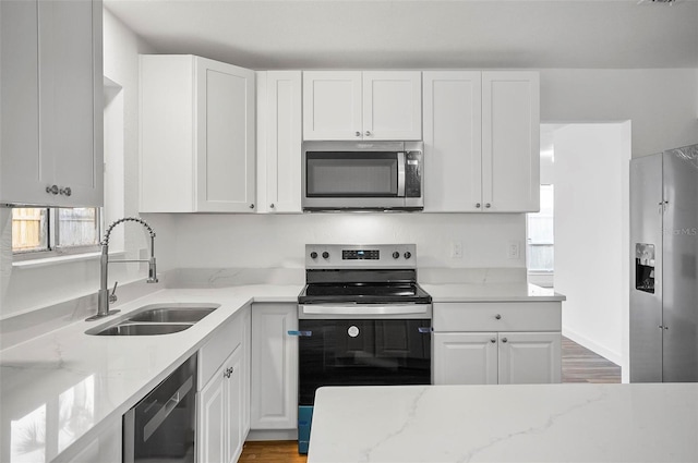 kitchen with sink, appliances with stainless steel finishes, white cabinetry, light stone counters, and light hardwood / wood-style floors