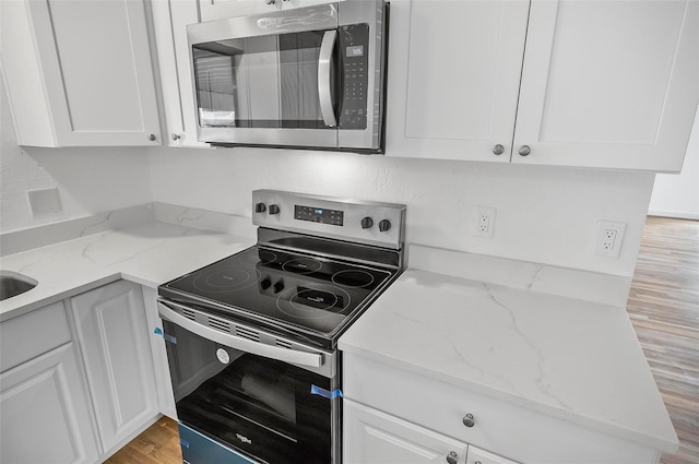 kitchen featuring light stone counters, stainless steel appliances, light hardwood / wood-style flooring, and white cabinets