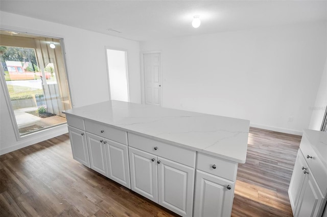 kitchen with wood-type flooring, a kitchen island, white cabinets, and light stone counters