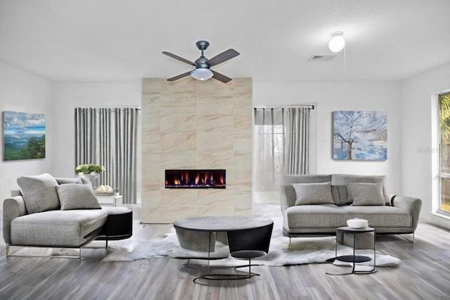 living room with a tiled fireplace, wood finished floors, visible vents, and ceiling fan