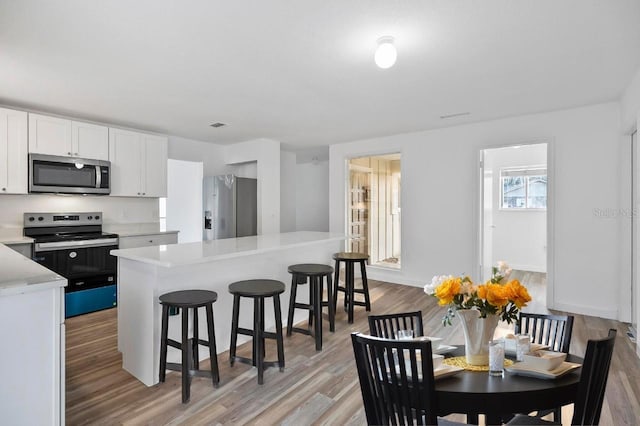 kitchen with stainless steel appliances, light countertops, white cabinetry, a kitchen breakfast bar, and light wood-type flooring