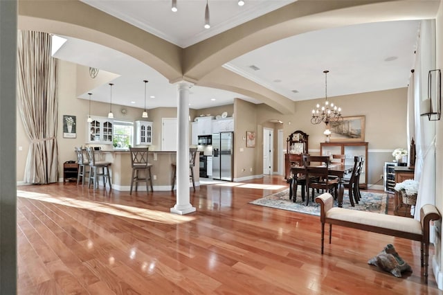 interior space featuring ornate columns, white cabinetry, decorative light fixtures, light wood-type flooring, and stainless steel fridge