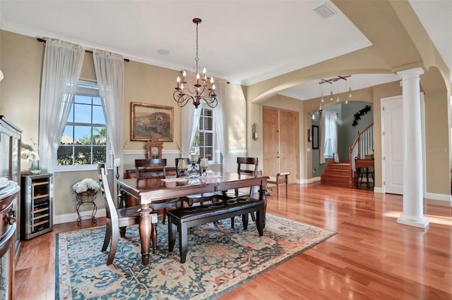 dining area with decorative columns, crown molding, hardwood / wood-style flooring, and beverage cooler