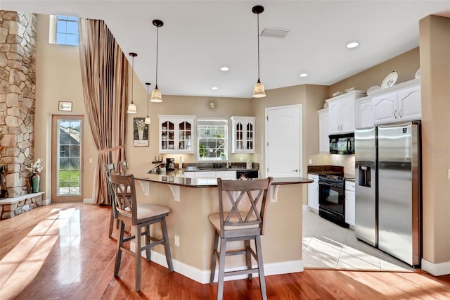 kitchen featuring a kitchen breakfast bar, light hardwood / wood-style floors, black appliances, white cabinets, and kitchen peninsula