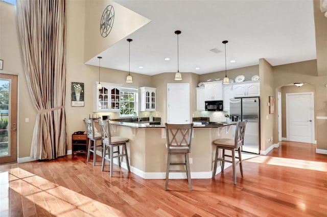 kitchen with decorative light fixtures, a breakfast bar, white cabinets, and stainless steel refrigerator with ice dispenser