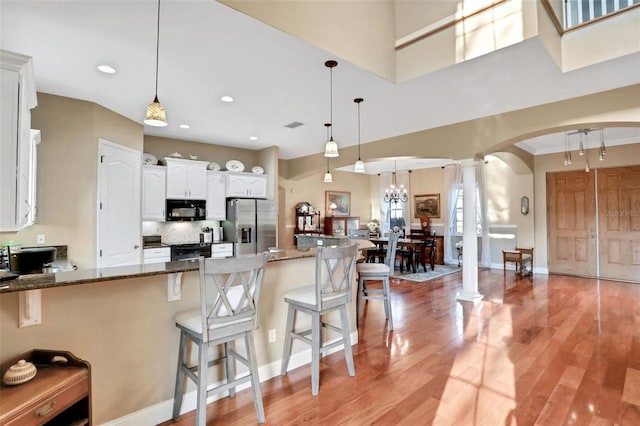 kitchen featuring white cabinets, dark stone countertops, hanging light fixtures, and black appliances