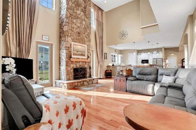 living room with a stone fireplace, light hardwood / wood-style floors, and a high ceiling