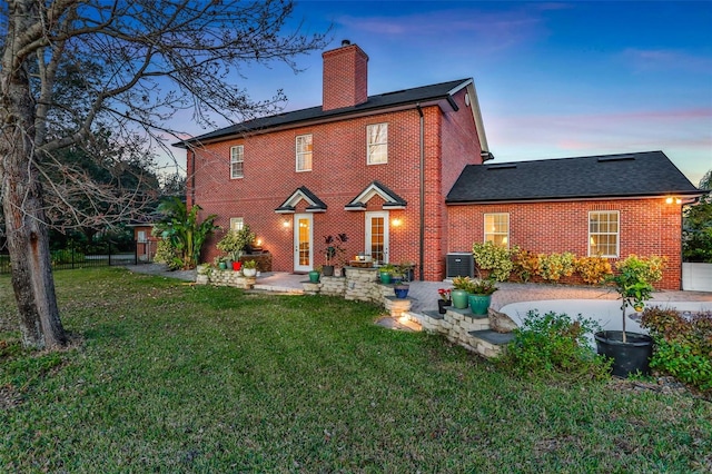 back house at dusk featuring a yard and a patio