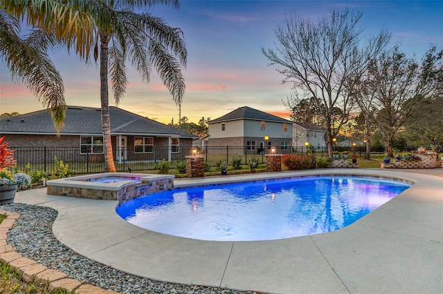 pool at dusk featuring an in ground hot tub and a patio