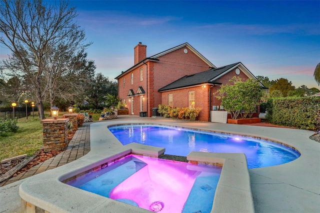 pool at dusk with an in ground hot tub