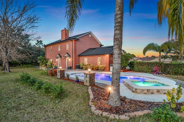 back house at dusk featuring a yard and a pool with hot tub