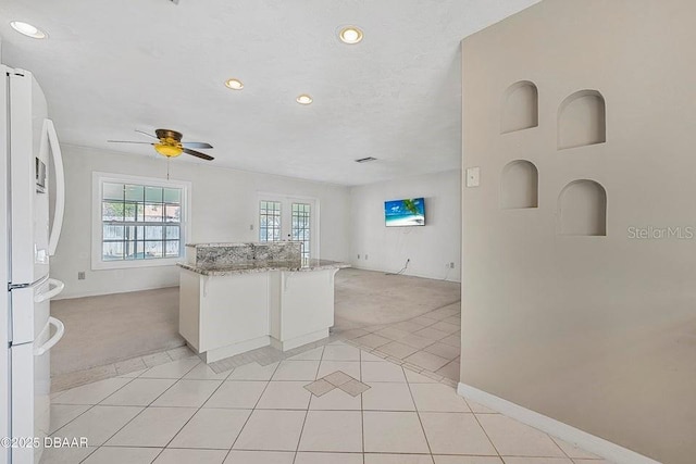 kitchen with light tile patterned flooring, white cabinetry, white fridge, ceiling fan, and light stone countertops