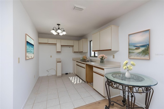 kitchen featuring pendant lighting, sink, light tile patterned floors, cream cabinets, and a notable chandelier