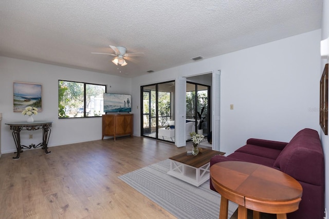 living room with ceiling fan, light hardwood / wood-style floors, and a textured ceiling