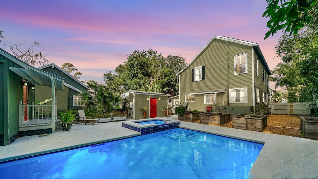 pool at dusk with a patio and an in ground hot tub